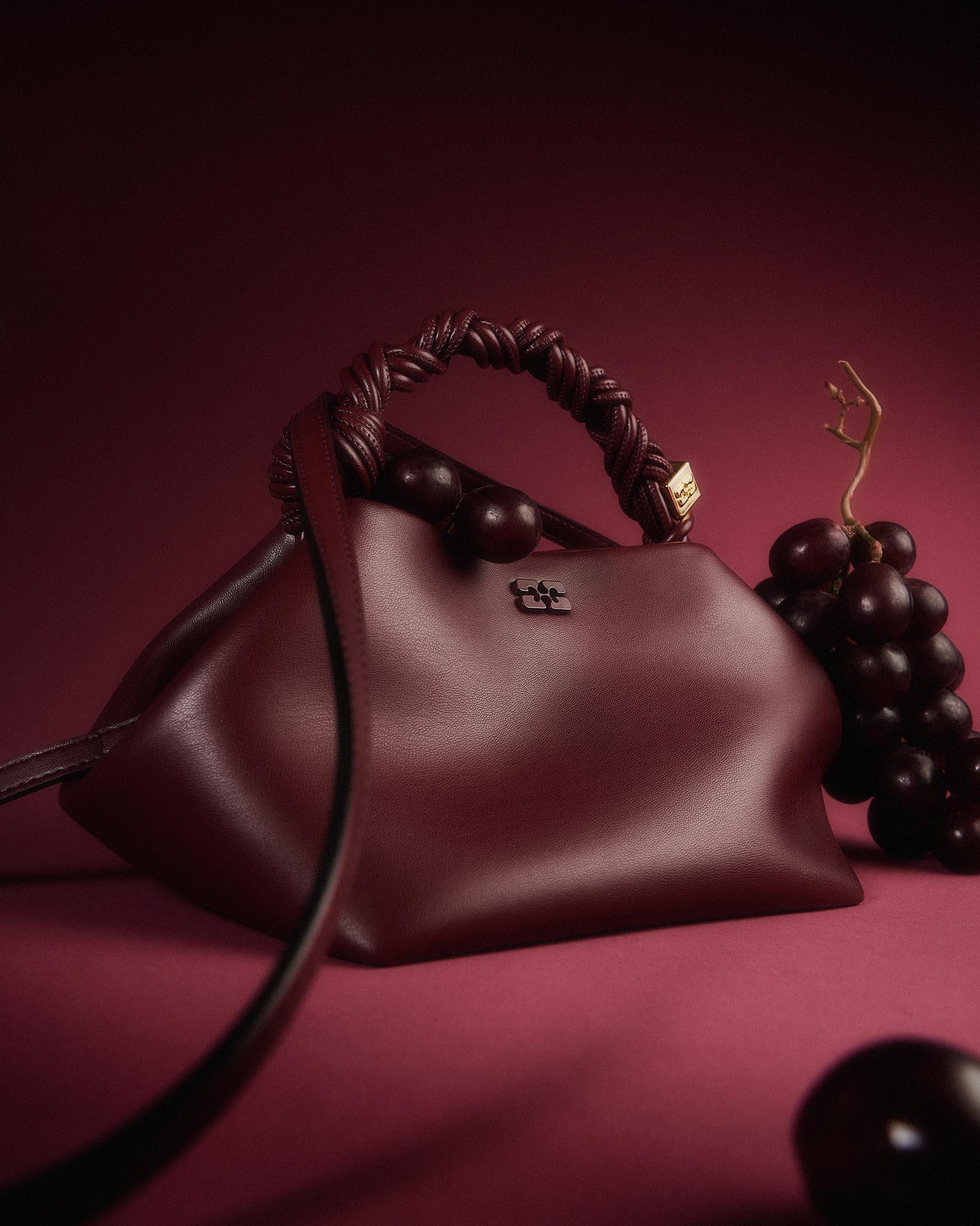 Sac en cuir bordeaux et raisins sur fond rouge, nature morte studio Shootime
