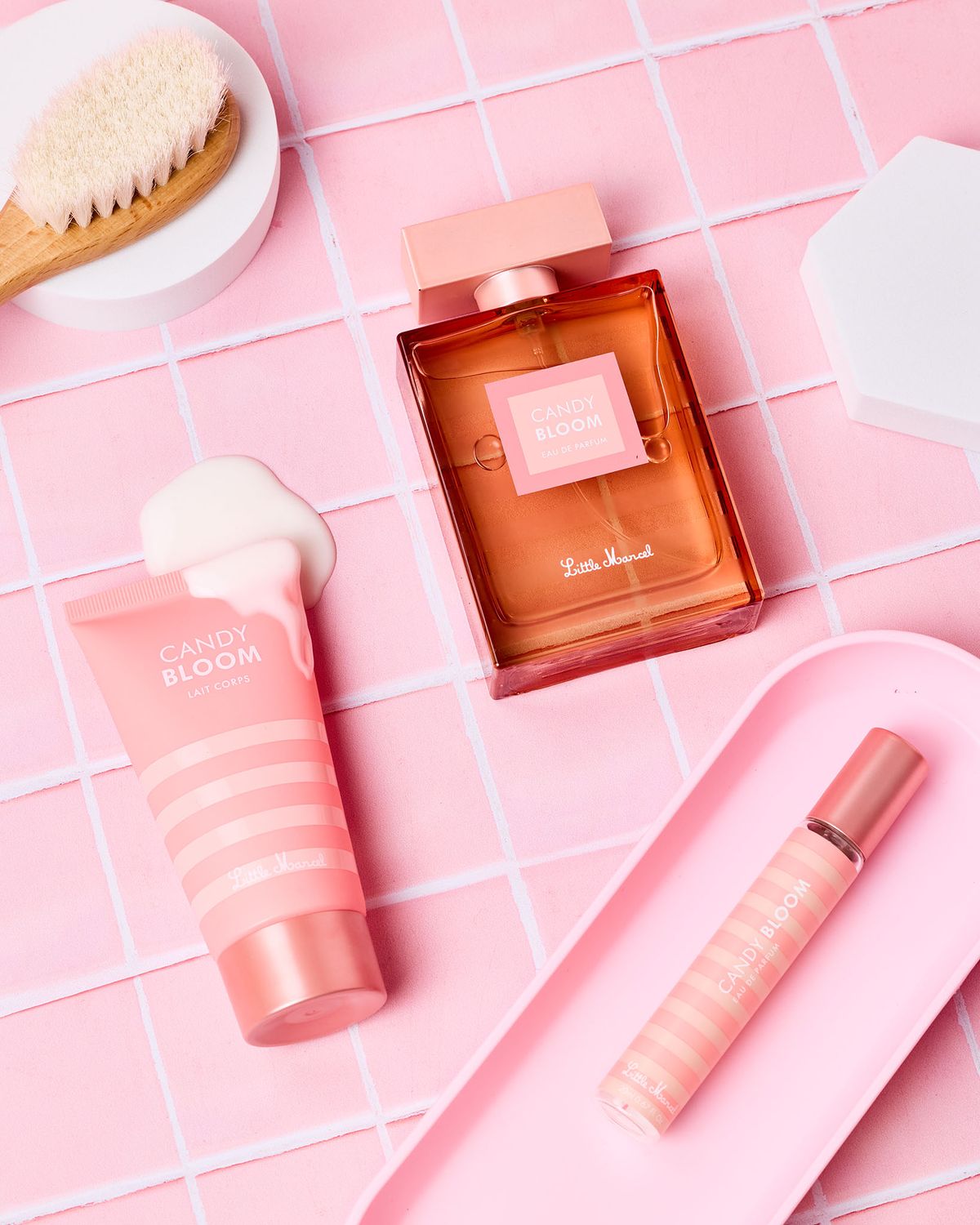 Sur une surface rose à motifs, il y a un parfum, une crème et un gloss à lèvres. Ces produits de beauté sont élégamment disposés, créant une ambiance douce et féminine.